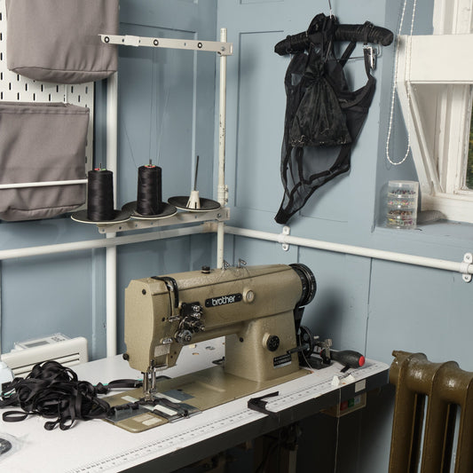 Sewing machine on the desk of a studio with a black bodysuit hung on a blue wall